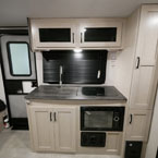 Kitchen Galley Area Shown with Two Cabinets Overhead of Sink, Two Burner Cook Top. Below Sink are Two Cabinet Doors and Microwave Next to Two Pantry Doors.
 May Show Optional Features. Features and Options Subject to Change Without Notice.